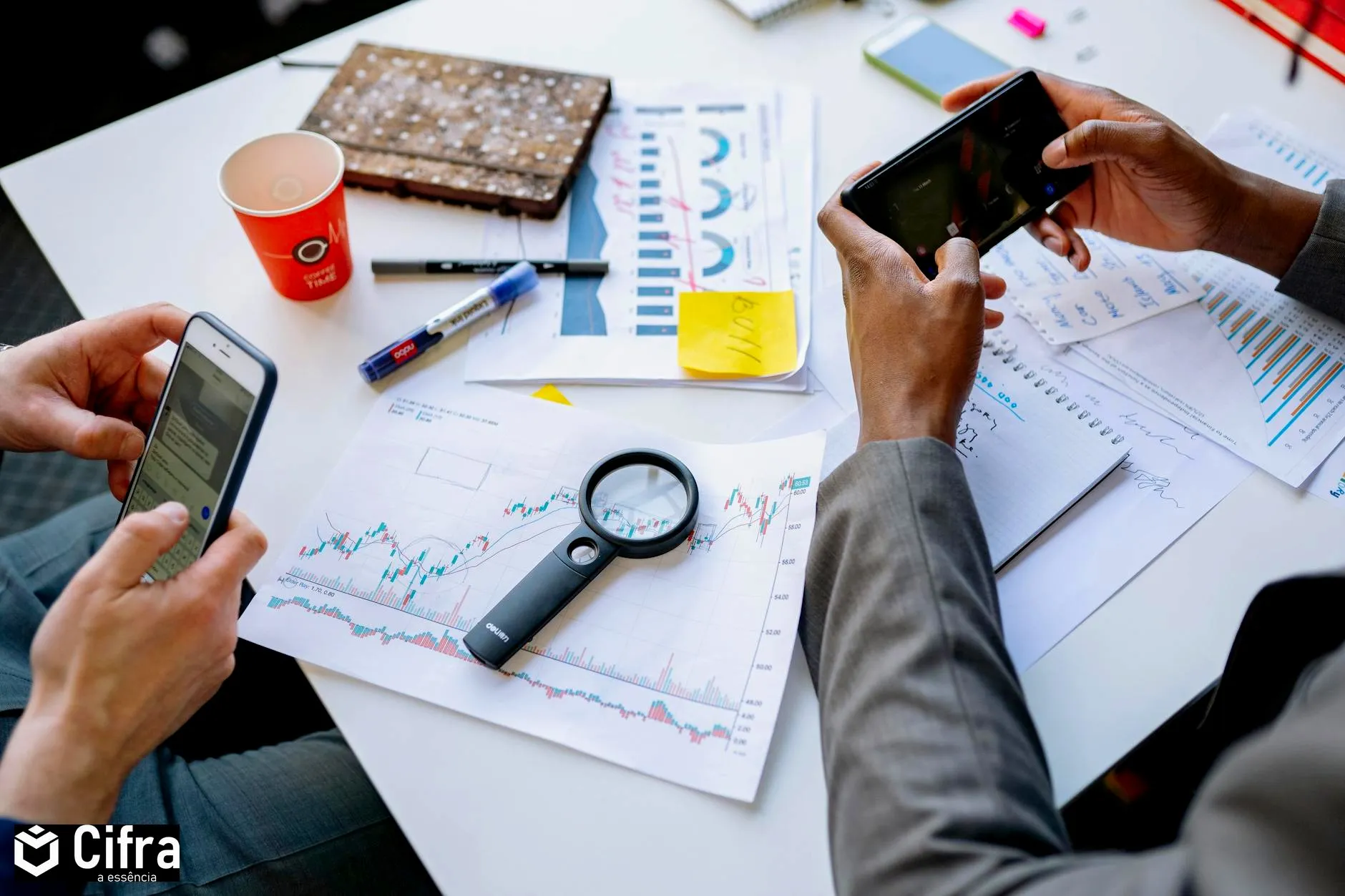 Two professionals analyzing data and graphs with smartphones on a white table.